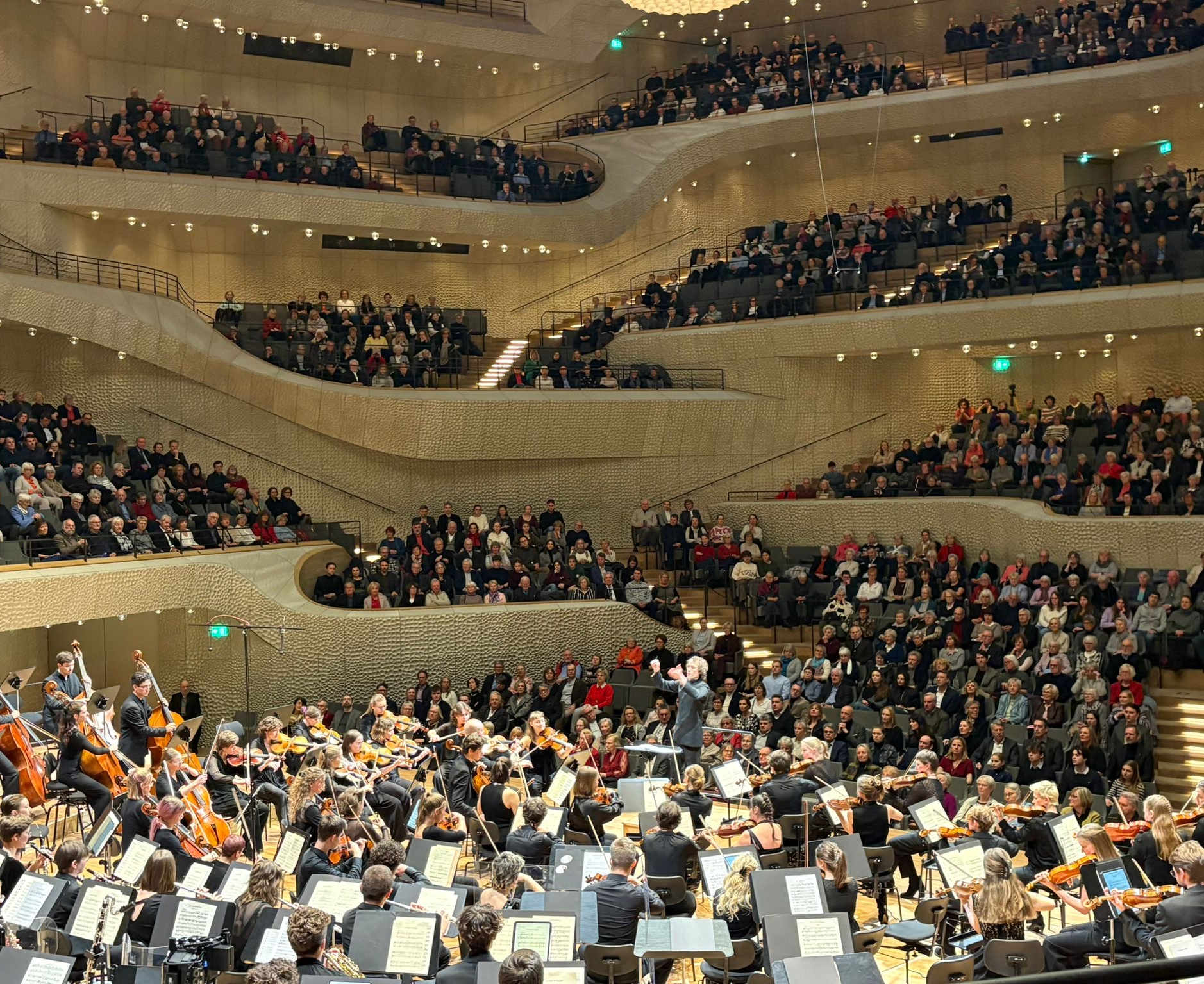 Orchester spielt im großen Saal der Elbphilharmonie, dahinter das voll besetzte Publikum